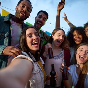 Students binge drinking alcohol party surrounded by group friends.